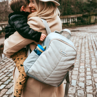 Babymel Gabby Backpack in Pale Grey worn by a mum carrying her child