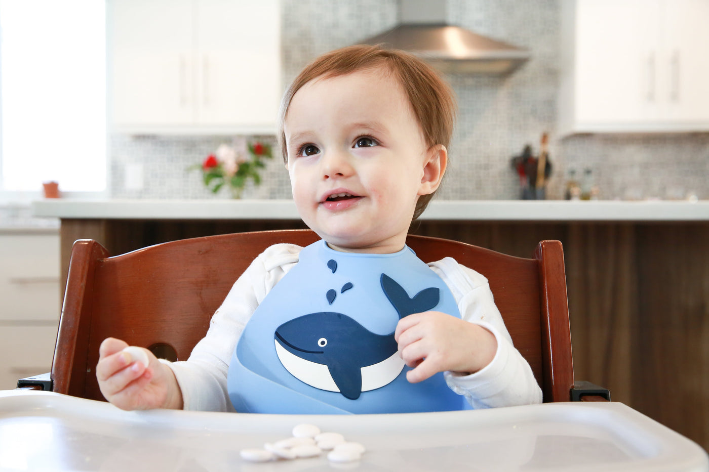Toddler in a high chair with a silicone bib on with a picture of a whale