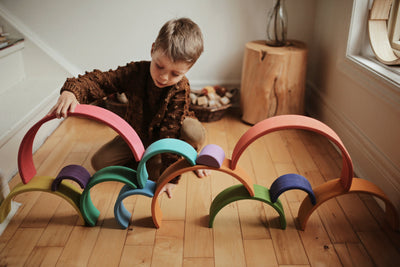 Boy playing with rainbow coloured wooden arches