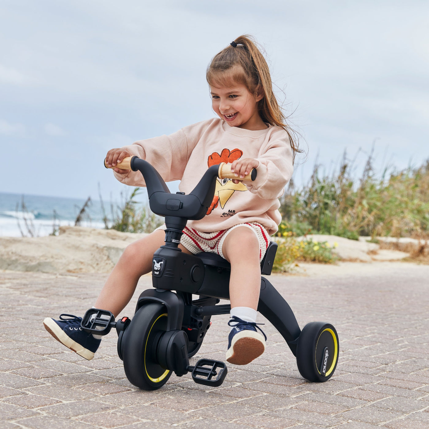 Child riding a tricycle on a paved path with a beach in the background