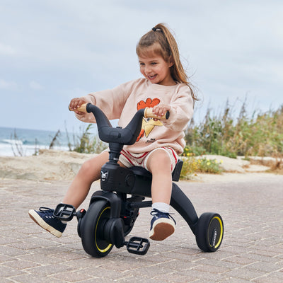 Child riding a tricycle on a paved path with a beach in the background