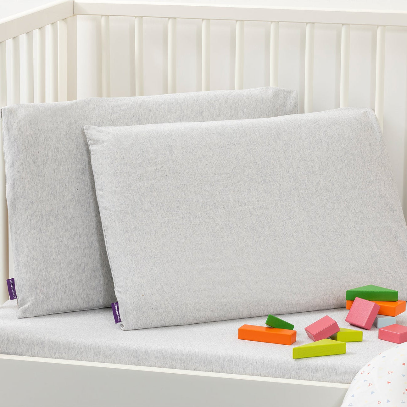 Gray pillows on a white crib with colorful blocks