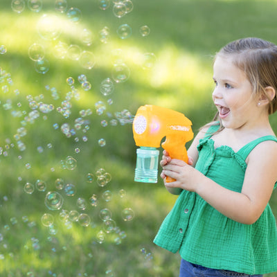 Child playing with a bubble gun outdoors, surrounded by bubbles.