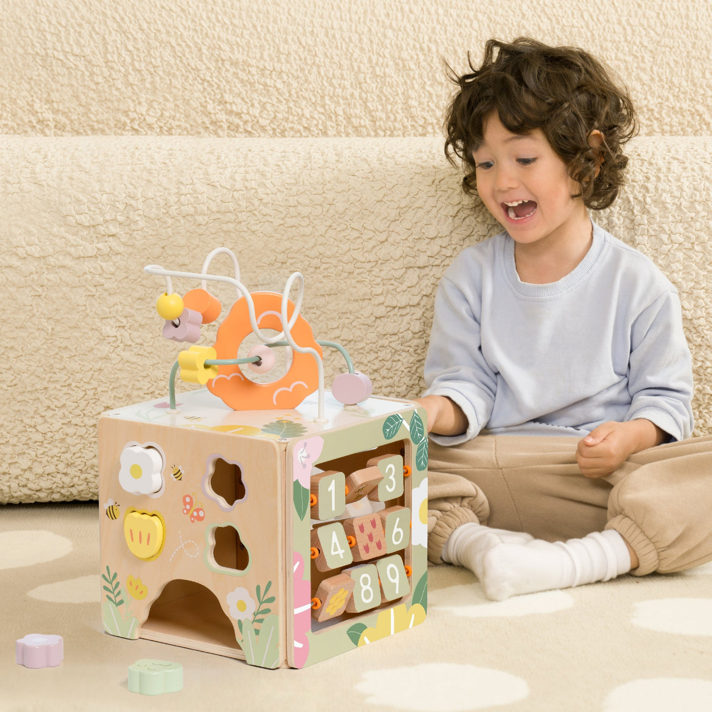 Child playing with a wooden toy that has numbers and shapes on a beige couch background