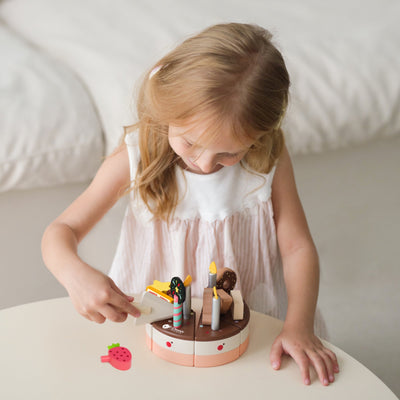 Young girl playing with a toy cake set on a table.