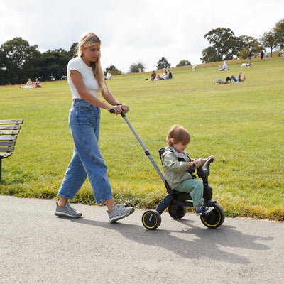 Woman pushing a child on a tricycle in a park