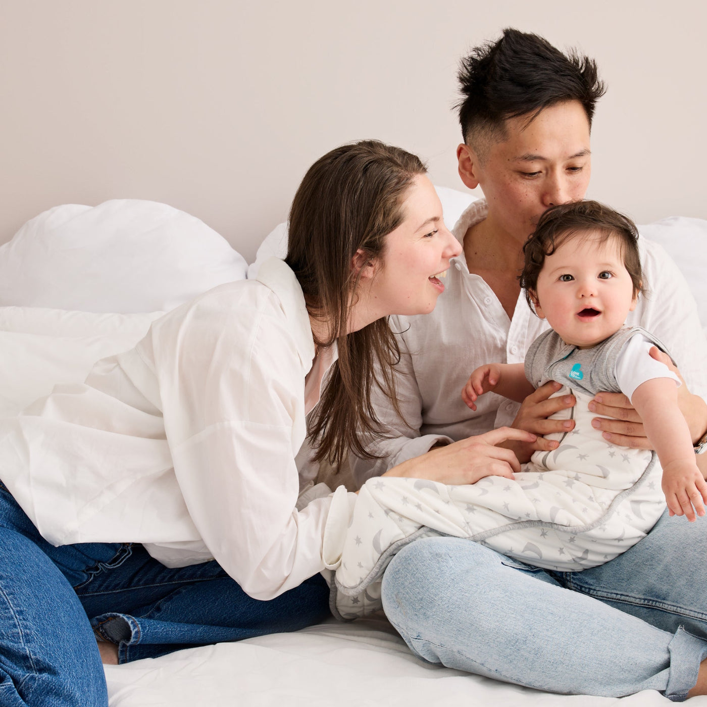 Family of three sitting on a bed, with a baby being held by the father.