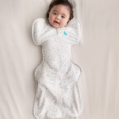 Baby lying on a beige blanket wearing a white sleep bag with small patterns.